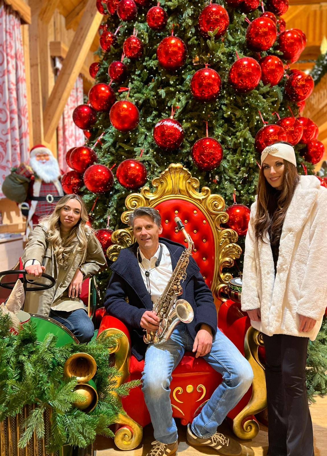 Judith und Sara zusammen mit Wolfram Dullnig von der Band "Saxolution" vor dem wundersch&ouml;n geschm&uuml;ckten Christbaum auf Gut Aiderbichl.