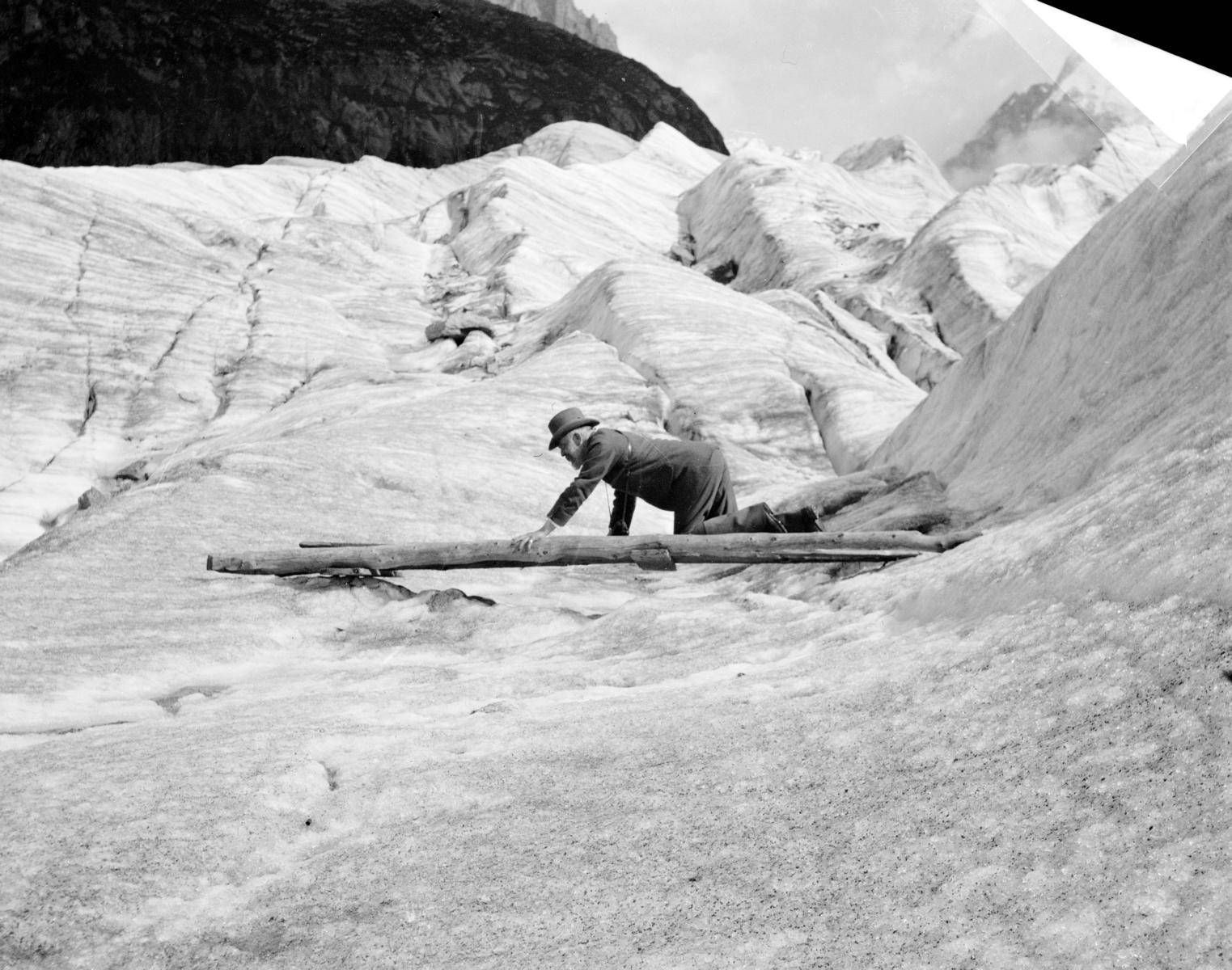 Grindelwald/Schweiz, 1901 &ndash; ein unbekannter Mann klettert auf einer Holzleiter &uuml;ber eine Eisplatte (Fotografin: Gertrude Bell)